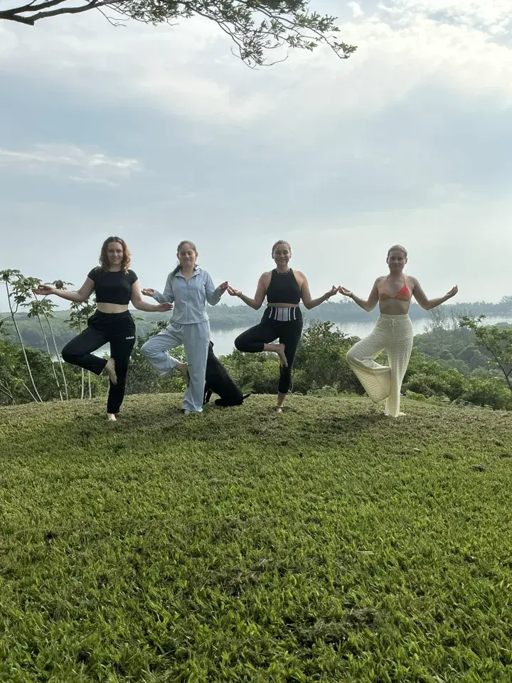 Cuatro mujeres practicando yoga al aire libre con la laguna y vegetación de Los Amigos al fondo